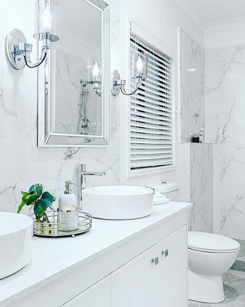 chrome wall lights in a white bathroom with marble walls