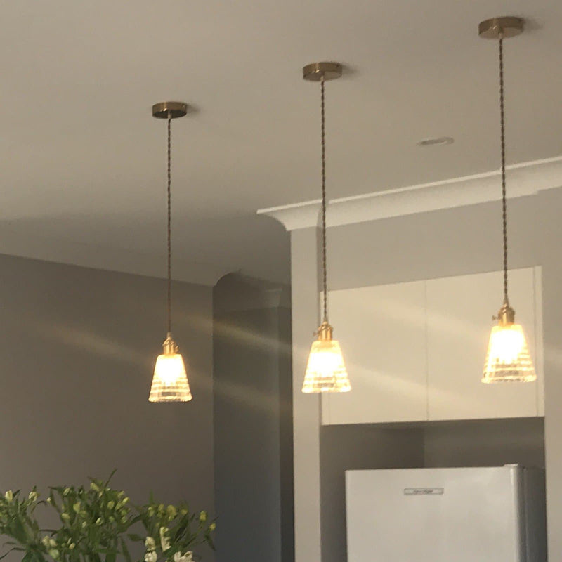 glass pendant light with gold hardware and textured tapered glass shade over a kitchen bench