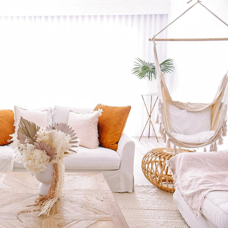 cream hammock hanging in a modern living room with orange cushions and cane side table