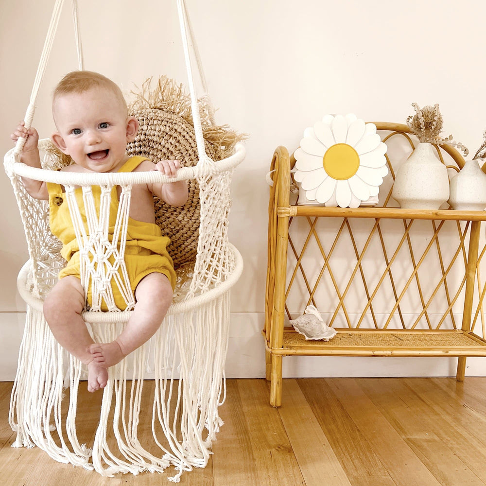 baby sitting in a macrame swing chair with yellow overalls