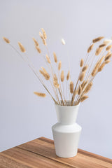 white ceramic vase with dried blossoms on a wooden table