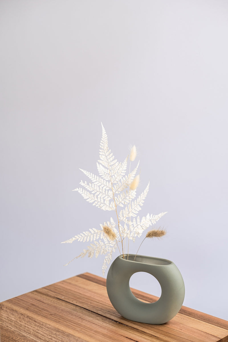 modern sage ceramic vase on a wooden shelf with dried leaves
